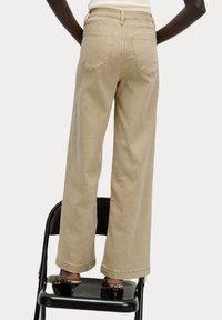 Bežové kalhoty s širokými nohavicemi vyrobené z měkké látky, s vysokým pasem, dvěma zadními kapsami a volným střihem s manžetami na spodním okraji.
