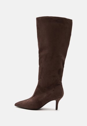 Botte femme en daim brun foncé montant jusqu'au genou avec bout pointu et talon fin de hauteur moyenne, vue de profil sur fond uni.