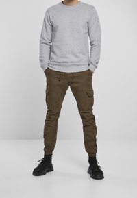 Sudadera gris con un cuello redondo, combinada con pantalones cargo verde oliva que tienen bolsillos y puños elásticos. Botas negras completan el conjunto.