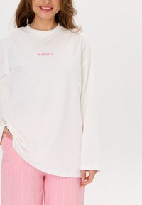 Witte lange mouw top met roze geborduurde tekst "MIRONS." Gecombineerd met lichtroze gestreepte wijde broek. Soepele stof, relaxed fit.