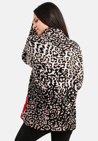 Leopardenmuster-Strickjacke in Schwarz und Hellbeige, mit einer strukturierten Strickoptik, Stehkragen und Seiten-Schlitzen für mehr Bewegungsfreiheit.