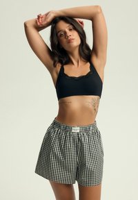 Czarny biustonosz z koronkowym wykończeniem połączony z szortami w czarno-białą kratkę. Tkanina jest gładka, szorty mają elastyczny pas.