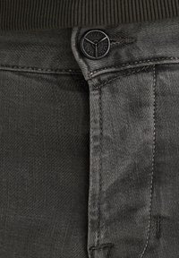 Sivé denim rifle s textúrovaným povrchom, so zapínaním na čierny gombík, jemným prešívaním a tmavým pásom, prezentujúc minimalistické dizajnové prvky.