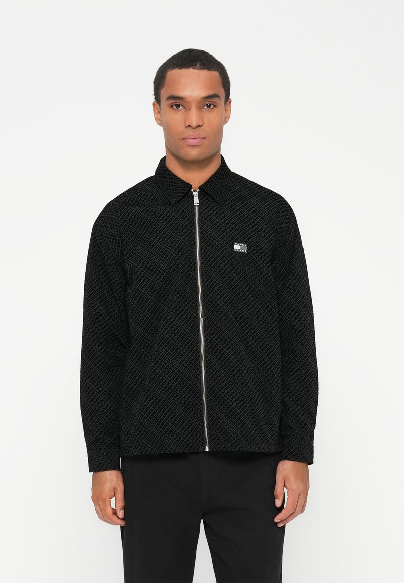 Juoda zip-up striukė su tekstūriniu deimantiniais raštais, smailiu apykakle ir mažuoju logotipo užnneriu ant kairiojo krūtinės. Ilgos rankovės su rankogaliais.