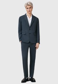 Ciemnoszary garnitur z jednorzędową marynarką i dopasowanymi spodniami. Cechy charakterystyczne: gładki materiał, klapy w kształcie szyjki oraz dopasowany krój.