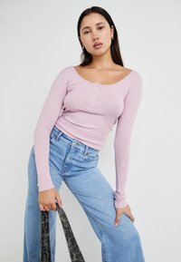 Lys lilla ribbet langermet topp med scoop-hals og knappdetaljer foran, kombinert med høytlivd lys blå jeans.