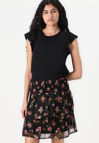 Svart kjole med volanger på ermene og en smocket blomsterkjole med lagdelte nivåer i røde, rosa og grønne blomster mønstre på svart bakgrunn.