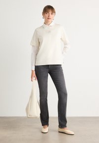 Top corto a maniche corte con colletto crema, jeans dritti grigi, ballerine beige e una borsa a spalla beige, con un design liscio e minimalista.