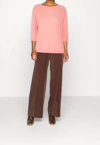 Jasnoróżowa bluzka z trzema czwartymi rękawami w połączeniu z brązowymi, szerokimi spodniami. Bluzka ma okrągły dekolt i miękką teksturę. Całość dopełniają skórzane botki za kostkę.