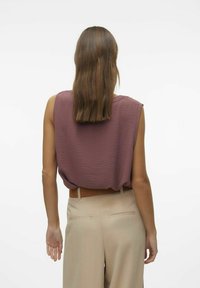 Lühikeste varrukatega laia lõikega pehme mauve värvi top, millel on peened lainelised tekstuurid, koos kõrge vöökoha ja beežide pükstega ning pruuni vööga.