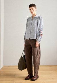 Ριγέ πουκάμισο με κεντημένα λουλούδια στα μανίκια, συνδυασμένο με καφέ παντελόνι, καφέ παπούτσια και πράσινη τσάντα.