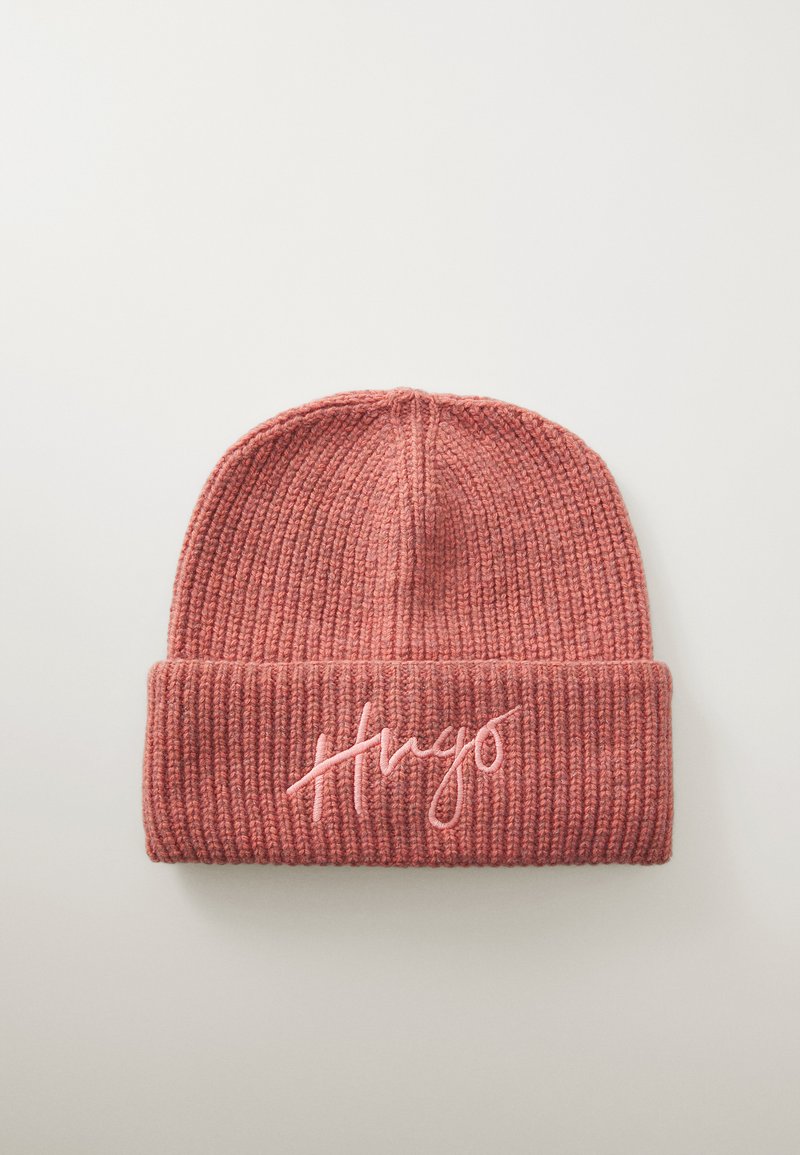 Pletena kapa v mehki rožnati barvi z rebrastim teksturo in zvit rim, z izvezenim napisom "Hugo" v svetlejši rožnati niti.