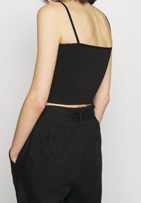 Svart ribbad kort tanktopp med tunna remmar, kombinerad med lösa svarta byxor med elastisk midja och sidofickor.