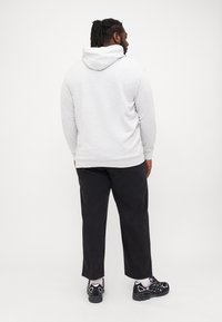 Grauer Hoodie mit einer weichen Textur und verstellbarer Kapuze, kombiniert mit schwarzen Hosen. Das Outfit wird durch schwarze Sneakers und weiße Knöchelsocken vervollständigt.