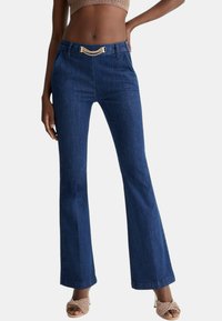 Jeans acampanados de color azul oscuro con un detalle de cadena dorada en la cinturilla. Hechos de tela de mezclilla con una textura suave y un corte ajustado.