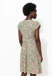 Robe à motifs floraux dans des tons de bleu, beige et orange. Présente des manches courtes et une taille cintrée pour souligner la silhouette. Texture de tissu douce.