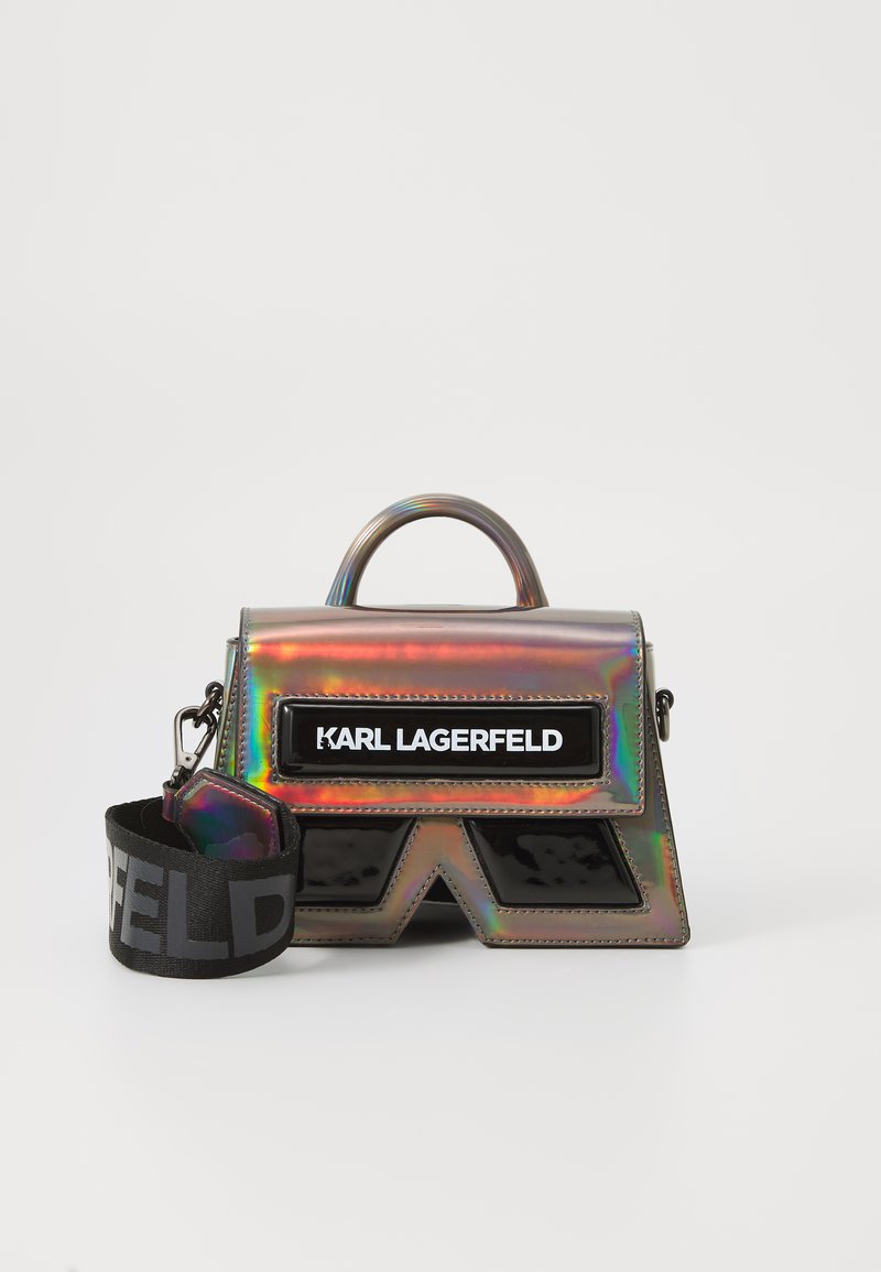 Iridiscent handbag with a structured shape, featuring a black logo patch, a glossy surface, and a detachable strap with bold lettering.
