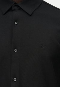 Μαύρο πουκάμισο με γιακά και κουμπιά μπροστά, με διακριτικό κεντημένο λογότυπο "cK" στο στήθος.