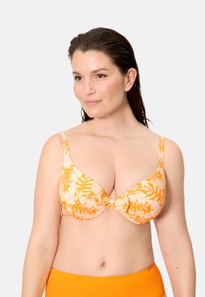 Mujer con el cabello mojado, lleva un bikini con top floral en tonos naranja y crema y una parte inferior naranja sólida, mirando ligeramente hacia un lado sobre un fondo liso.
