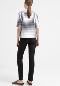 Pruhovaný top s krátkým rukávem v námořnické modré a bílé barvě, doplněný o černé slim kalhoty a černé slip-on sandály.