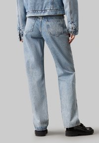 Jeans de mezclilla azul claro con corte recto, cinco bolsillos y un lavado desgastado. Combinados con una chaqueta de mezclilla a juego y zapatos de plataforma negros.