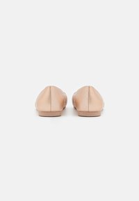 Ballerines beiges avec une finition lisse, bout rond, petit talon et couture discrète à l'arrière. Design simple sans ornement.