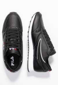 Sneakers nere in materiale sintetico con una texture liscia, dotate di lacci neri, suola bianca e sottili accenti argento sui lati.