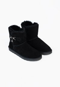 Bottines noires à la cheville avec doublure intérieure en fourrure douce, semelle plate en caoutchouc, et boucle latérale décorative ornée de petits charms en métal.