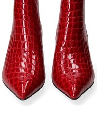 Stivaletti alla caviglia in pelle verniciata rossa con punta affusolata, caratterizzati da una texture in pelle di coccodrillo e una finitura lucida e elegante. Suole nere e senza hardware visibile.