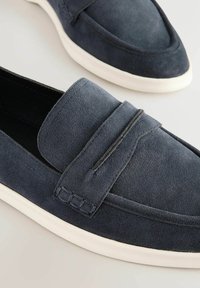 Tmavomodré semišové loafer sandále s okrúhlou špičkou, prešitými detailmi a bielou gumovou podrážkou. Majú jednoduchý dizajn na obúvanie s minimálnymi detailmi.