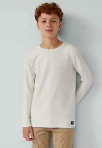 Langarm T-shirt met ronde hals in off-white katoen, voorzien van een klein zwart logo label nabij de zoom. Soepele textuur, casual pasvorm.