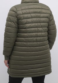 Oliivinvihreä toppatakki, jossa tikattu kuvio, korkea kaulus ja resorit hihansuissa. Takissa on puolipitkä leikkaus ja sileä, kiiltävä pinta.