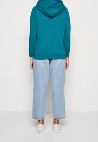 Sweat-shirt à capuche turquoise à coupe décontractée, associé à un jean droit délavé clair avec des ourlets effilochés et des baskets blanches.