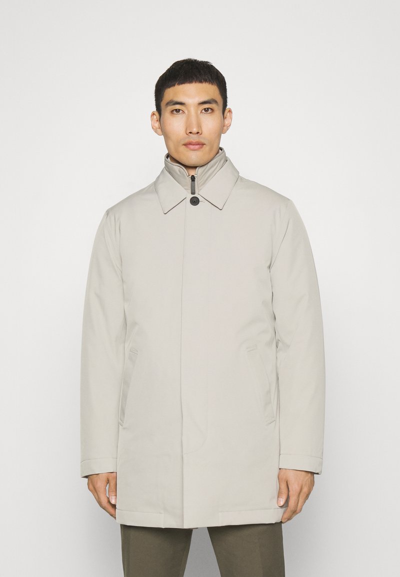 Abrigo impermeable beige claro con un cuello alto, botones delanteros y bolsillos laterales. Textura suave y diseño recto.