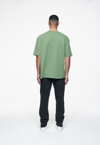 Green short-sleeve t-shirt made of cotton, featuring a relaxed fit and minimalistic design, paired with dark jeans and white sneakers.