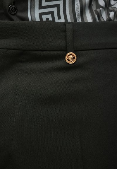 Μαύρο παντελόνι από ύφασμα με λεία υφή, διαθέτ�ει χρυσό κουμπί με έμβλημα λιονταριού και θηλιά για ζώνη στη μέση.