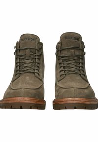 Bruna mocka ankelstövlar med rund tå, snörningsdesign och gummisulor. Har en sydd tåkappa och en upphöjd logotyp på tungan.