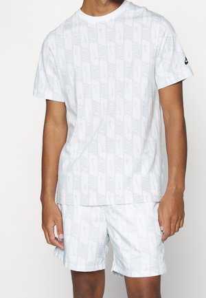 Sada bílého trička a šortek s opakujícím se světle šedým vzorem loga Nike, krátké rukávy, kulatý výstřih a elastický pas.