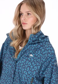 Kék leopárdmintás kapucnis dzseki cipzárral és patentos záródással, sima tapintású, bal mellrészen logóval.