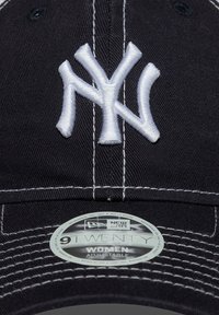 Svart stoff baseballcap med hvit brodert "NY"-logo, med kontraststing, justerbar stropp og rund størrelseetikett inni.