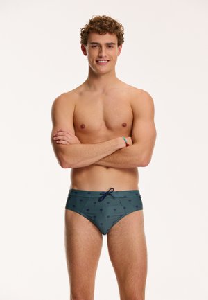Bañadores ajustados de hombre en color verde oscuro con patrón de palmeras. Presentan una cintura con cordón y una textura de tela suave.