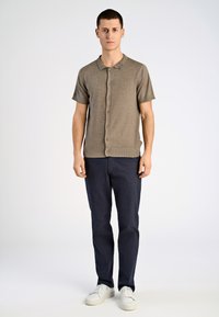 Kortärmad, ljusbrun stickad polo med knäppning fram, kombinerad med mörkblå byxor och vita sneakers. Slät yta, avslappnad passform.
