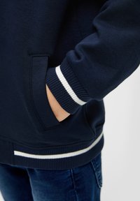 Felpa navy con polsini e orlo a costine, decorata con strisce bianche. Tasca laterale visibile, realizzata in morbido cotone. Design classico a girocollo.