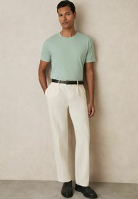 Tricou scurt, de culoare verde deschis, asortat cu pantaloni crem și o curea neagră. Pantofii negri completează ținuta, având o croială ajustată.