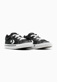 Zapatillas de lona negras con suelas de goma blancas, que cuentan con cordones blancos y un logotipo contrastante en el lateral. Parte superior texturizada con acentos contrastantes.