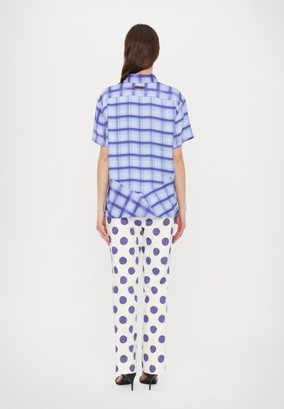 Camicia a maniche corte a quadri blu abbinata a pantaloni bianchi con grandi pois viola. La camicia presenta un colletto e un design unico sul pannello frontale.