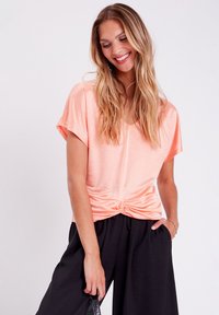 Haut court pêche à manches courtes avec un col en V et un détail noué à la taille, fabriqué en tissu doux, associé à un pantalon noir ample.