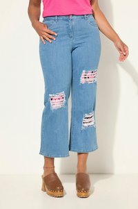Ljusblå denimbyxor med vida ben och slitna knäpartier som avslöjar rosa och svarta randiga tyger. Sitter åtsittande i midjan och har en lätt fransad fåll.