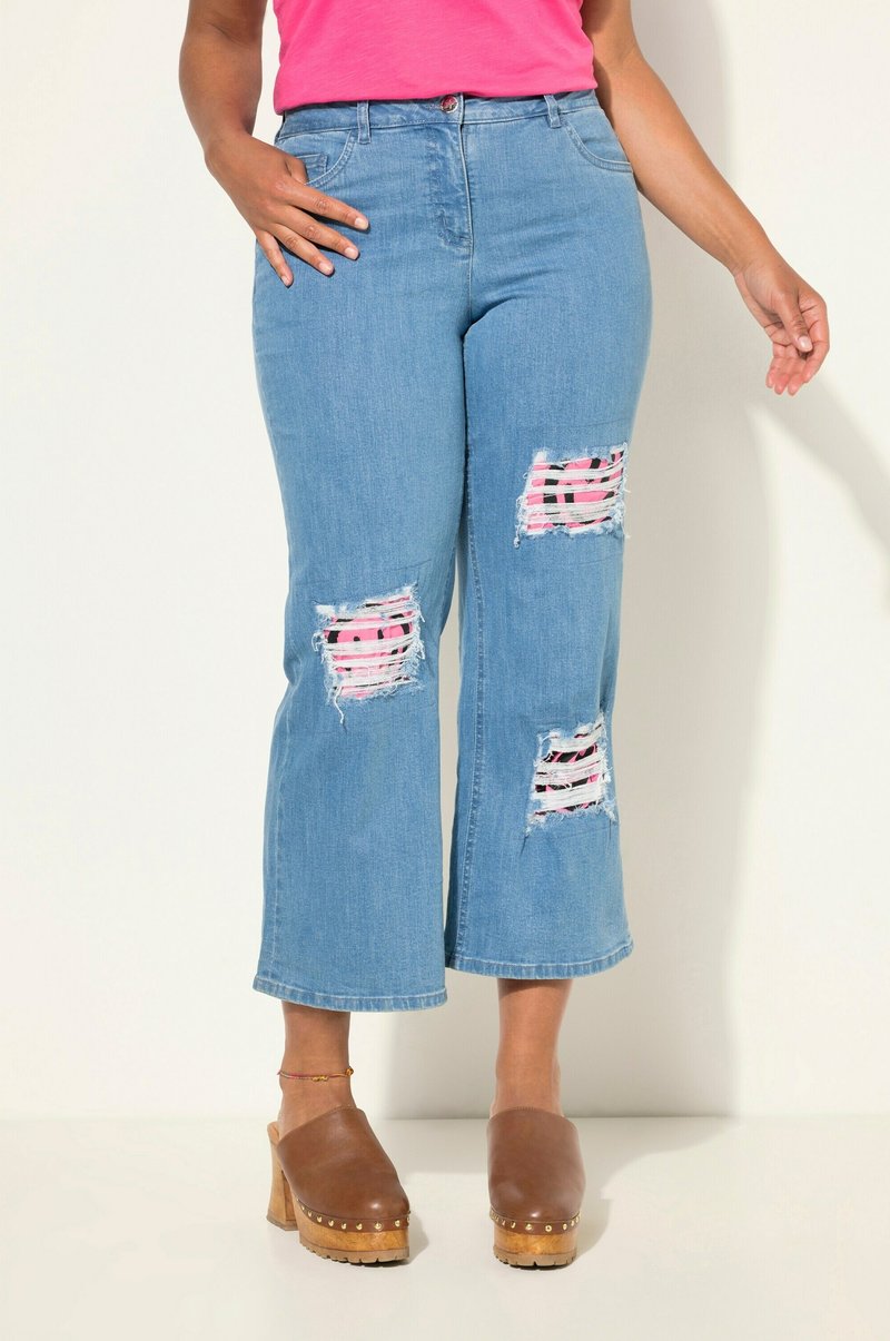 Ljusblå denimbyxor med vida ben och slitna knäpartier som avslöjar rosa och svarta randiga tyger. Sitter åtsittande i midjan och har en lätt fransad fåll.