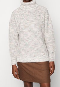 Chunky gebreide trui in lichte tinten met een col, voorzien van een textuurpatroon en geribbelde manchetten, gecombineerd met een bruine rok.